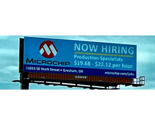 A light blue billboard for Microchip that reads 'Now Hiring, Production Specialists, $19.68 - $22.12 per hour'